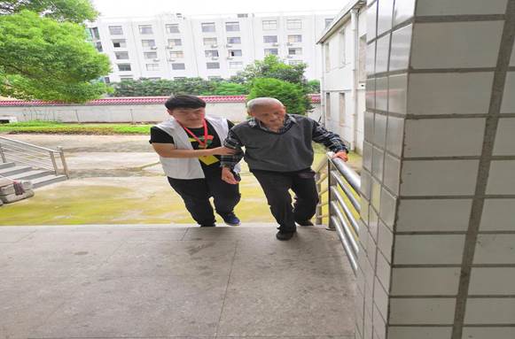 說明:志愿者梁亞東扶王三娃爺爺上樓梯